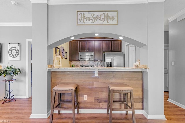 3101 Bridgewater Dr, Carrollton, VA 23314 - kitchen featuring appliances with stainless steel finishes, crown molding, wood finished floors, dark brown cabinets, and a kitchen bar