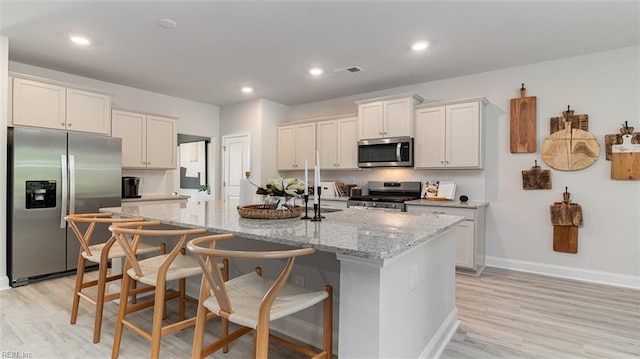 1228 Kidbrooke St, Chesapeake, VA 23322 - kitchen featuring appliances with stainless steel finishes, a center island with sink, decorative backsplash, light wood-style flooring, and a kitchen bar