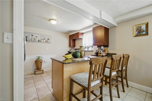 5133 E Princess Anne Rd, Norfolk, VA 23502 - kitchen featuring a peninsula, light tile patterned floors, a breakfast bar, dark stone countertops, and wainscoting