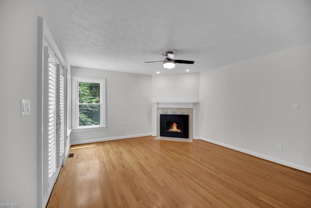 105 Londonderry Ln, Williamsburg, VA 23188 - unfurnished living room featuring ceiling fan, a tiled fireplace, light wood finished floors, baseboards, and a textured ceiling