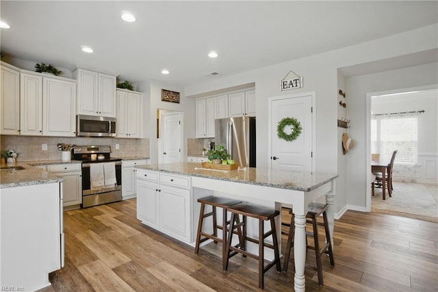 2685 Robert Monette Ln, Virginia Beach, VA 23456 - kitchen with appliances with stainless steel finishes, light wood-style flooring, a center island, decorative backsplash, and a breakfast bar area