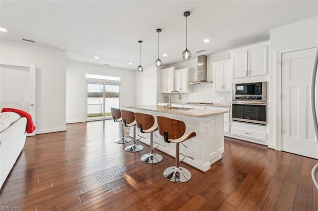 1652 Teton Ct, Chesapeake, VA 23320 - kitchen featuring stainless steel appliances, wall chimney exhaust hood, a sink, white cabinetry, and a kitchen bar