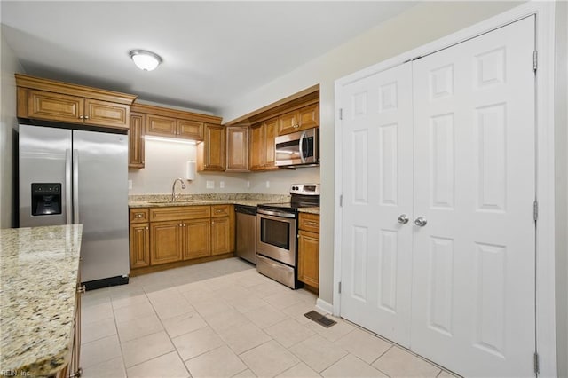 2613 Cedar Rd, Chesapeake, VA 23323 - kitchen featuring appliances with stainless steel finishes, a sink, brown cabinetry, light stone counters, and light tile patterned floors