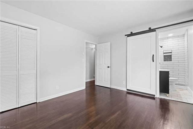 313 Delk St, Franklin, VA 23851 - unfurnished bedroom with wood finished floors, a barn door, baseboards, ensuite bathroom, and a closet