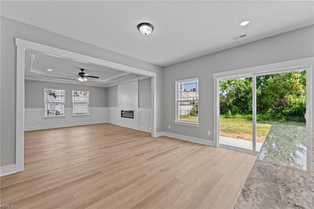 4 Roundtree Cir, Hampton, VA 23661 - unfurnished living room featuring light wood finished floors, plenty of natural light, ceiling fan, a tray ceiling, and a wainscoted wall