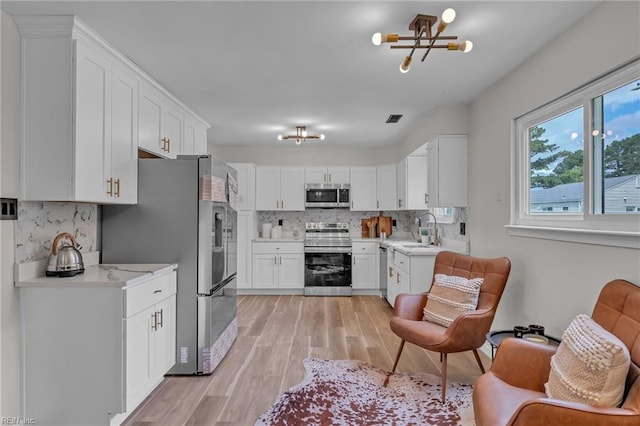 2920 Fetsch Pl, Virginia Beach, VA 23453 - kitchen with stainless steel appliances, light wood-type flooring, tasteful backsplash, white cabinetry, and a chandelier