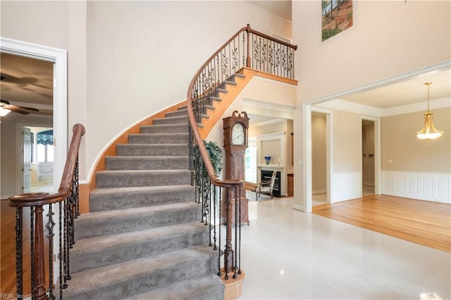 5225 Regatta Pointe Rd, Suffolk, VA 23435 - staircase featuring tile patterned flooring, crown molding, a wainscoted wall, ceiling fan, and a towering ceiling