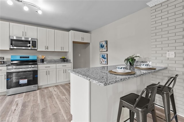 1309 Wickham Ave, Newport News, VA 23607 - kitchen with appliances with stainless steel finishes, a kitchen breakfast bar, light wood-type flooring, light stone counters, and white cabinetry