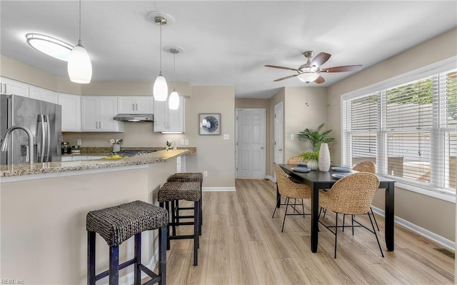 1304 Glen Burnie Ct, Virginia Beach, VA 23454 - kitchen with stainless steel fridge with ice dispenser, under cabinet range hood, white cabinetry, a breakfast bar area, and light wood finished floors