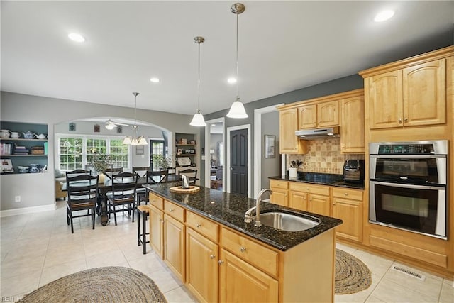 2316 Holland Rd, Virginia Beach, VA 23453 - kitchen featuring stainless steel double oven, under cabinet range hood, a kitchen island with sink, decorative backsplash, and dark stone countertops