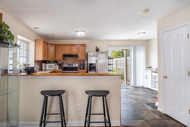 5537 Port Royal Dr, Virginia Beach, VA 23462 - kitchen featuring appliances with stainless steel finishes, under cabinet range hood, a peninsula, a kitchen breakfast bar, and backsplash