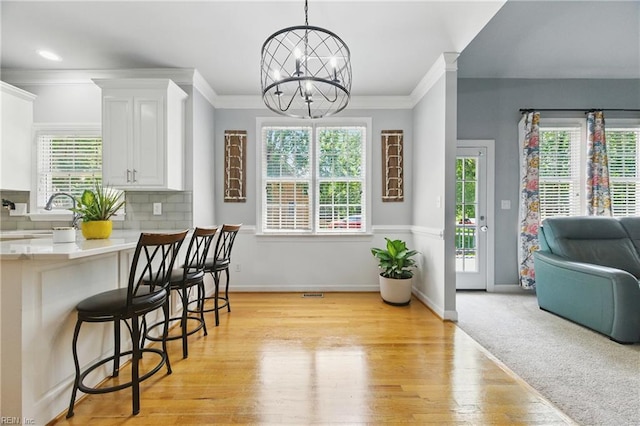 20517 Madison Ct, Smithfield, VA 23430 - kitchen with a chandelier, a breakfast bar, plenty of natural light, white cabinetry, and ornamental molding