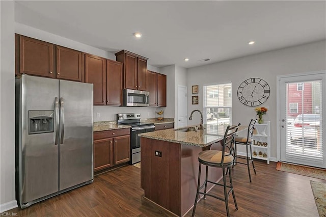 4321 Sconce, Williamsburg, VA 23188 - kitchen with appliances with stainless steel finishes, a kitchen breakfast bar, dark wood-style flooring, light stone counters, and an island with sink