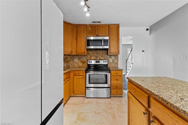 114 Lancelot Dr, Suffolk, VA 23434 - kitchen featuring appliances with stainless steel finishes, backsplash, brown cabinetry, light stone countertops, and a textured ceiling