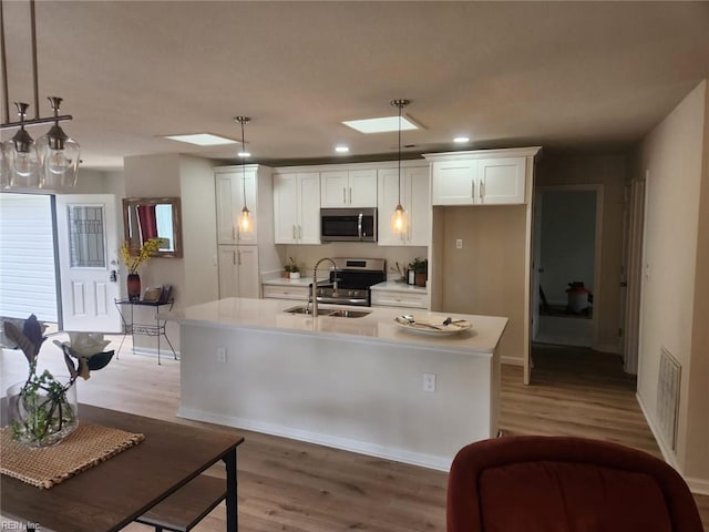 13031 Green Grove Ln, Newport News, VA 23608 - kitchen with appliances with stainless steel finishes, white cabinets, light countertops, light wood-style floors, and a kitchen island with sink