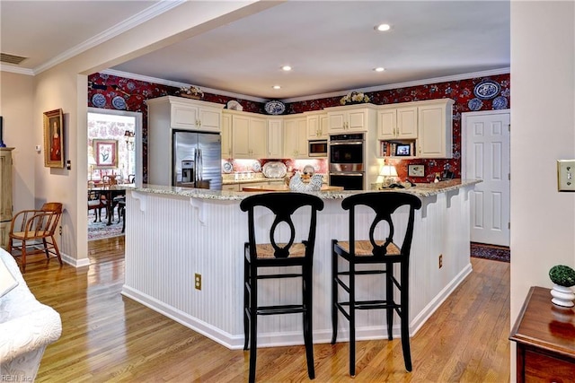 8265 Wrenfield Dr, Williamsburg, VA 23188 - kitchen featuring appliances with stainless steel finishes, light wood finished floors, ornamental molding, a breakfast bar area, and light stone counters