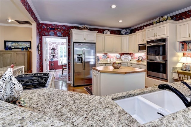 8265 Wrenfield Dr, Williamsburg, VA 23188 - kitchen featuring appliances with stainless steel finishes, ornamental molding, wallpapered walls, white cabinetry, and a kitchen island