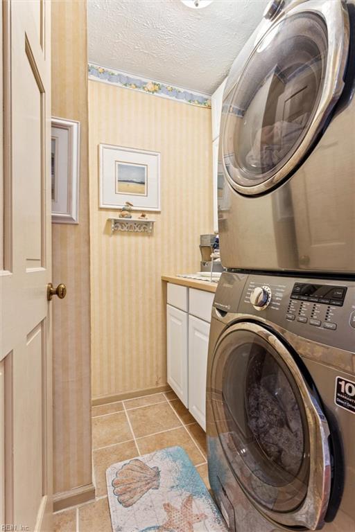 102 Canvasback Trl, Newport News, VA 23602 - laundry room featuring stacked washer and clothes dryer, cabinet space, wallpapered walls, a textured ceiling, and light tile patterned floors