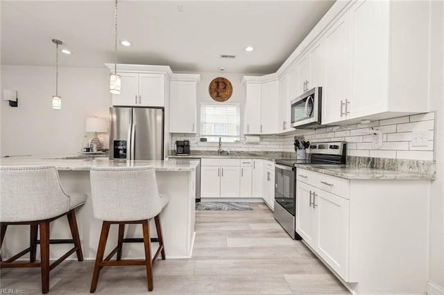 401 W 30th St, Norfolk, VA 23508 - kitchen featuring appliances with stainless steel finishes, a breakfast bar area, white cabinets, decorative backsplash, and pendant lighting