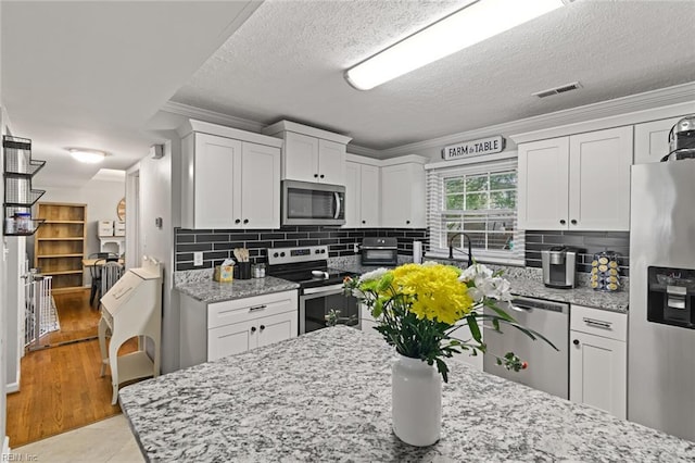 102 Dogwood Dr, Williamsburg, VA 23185 - kitchen featuring appliances with stainless steel finishes, ornamental molding, white cabinets, light stone countertops, and backsplash