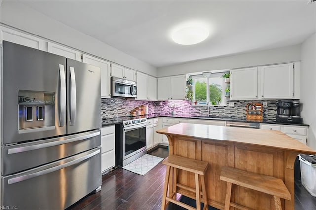 1712 Willwood Ct, Virginia Beach, VA 23464 - kitchen with appliances with stainless steel finishes, dark wood-style flooring, decorative backsplash, white cabinetry, and a kitchen breakfast bar