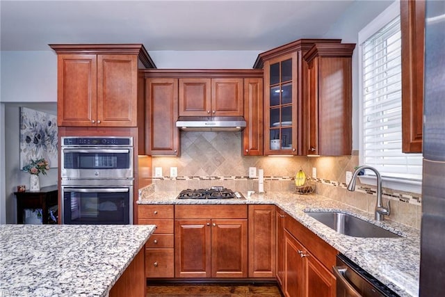 6355 Cordelia Rd, Williamsburg, VA 23188 - kitchen featuring appliances with stainless steel finishes, under cabinet range hood, light stone counters, backsplash, and glass insert cabinets