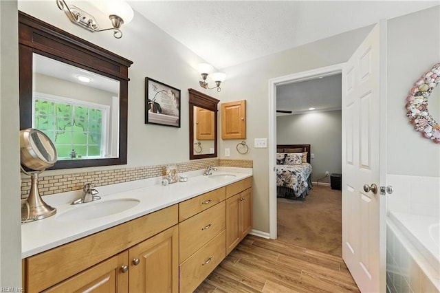 2152 Benomi Dr, Williamsburg, VA 23185 - ensuite bathroom featuring wood finished floors, a bath, double vanity, backsplash, and a textured ceiling