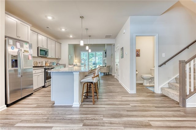 2207 Fallon Cir, Williamsburg, VA 23188 - kitchen with appliances with stainless steel finishes, light wood-style flooring, a breakfast bar, a center island with sink, and hanging light fixtures