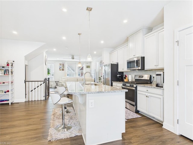 1732 Defiance Dr, Chesapeake, VA 23323 - kitchen with stainless steel appliances, a breakfast bar area, an island with sink, white cabinetry, and dark wood-style flooring