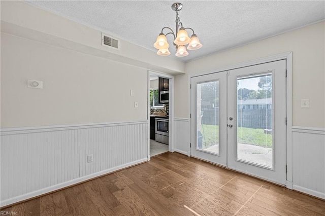 596 Old Post Rd, Virginia Beach, VA 23452 - unfurnished dining area with wood finished floors, a chandelier, a wainscoted wall, french doors, and a textured ceiling