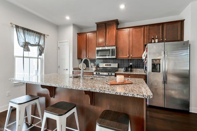 1803 Yardarm Way, Chesapeake, VA 23323 - kitchen featuring appliances with stainless steel finishes, dark wood-type flooring, backsplash, a center island with sink, and light stone countertops