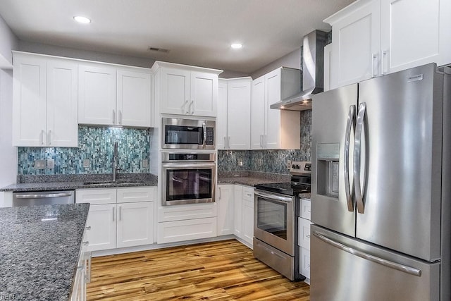 1161 Bells Mill Rd, Chesapeake, VA 23322 - kitchen featuring appliances with stainless steel finishes, wall chimney range hood, white cabinetry, light wood finished floors, and dark stone counters