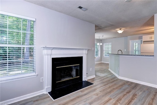 3957 Driftwood Way, Williamsburg, VA 23188 - unfurnished living room featuring a textured ceiling, light wood-type flooring, a fireplace with flush hearth, and a chandelier