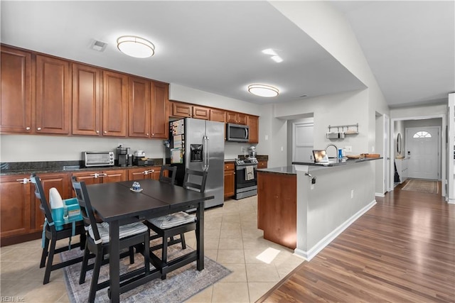 4052 Peridot Dr, Virginia Beach, VA 23456 - kitchen featuring stainless steel appliances, dark countertops, a peninsula, brown cabinetry, and light tile patterned floors
