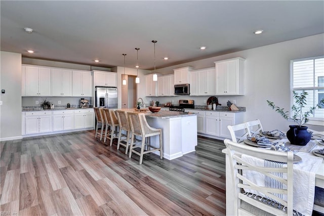 9116 Daydreamer Ct, Toano, VA 23168 - kitchen featuring stainless steel appliances, white cabinets, light wood-type flooring, light stone countertops, and an island with sink
