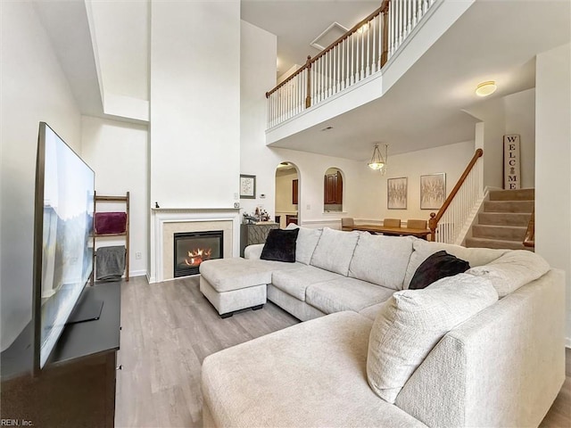 4208 Falcon Creek Dr, Williamsburg, VA 23188 - living area featuring arched walkways, wood finished floors, a towering ceiling, stairway, and a glass covered fireplace