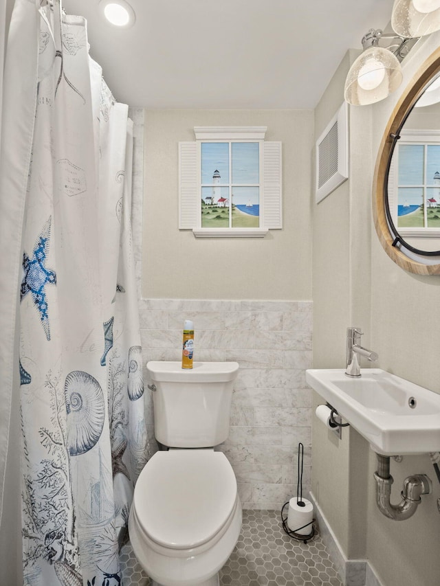 bathroom featuring toilet, sink, tile walls, a wealth of natural light, and tile patterned flooring