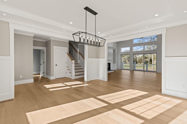 unfurnished living room with wood-type flooring, a large fireplace, crown molding, and a chandelier