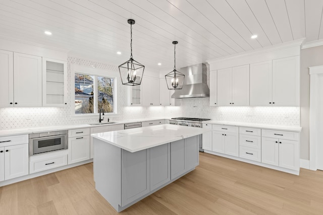 kitchen with appliances with stainless steel finishes, white cabinetry, sink, a kitchen island, and wall chimney exhaust hood