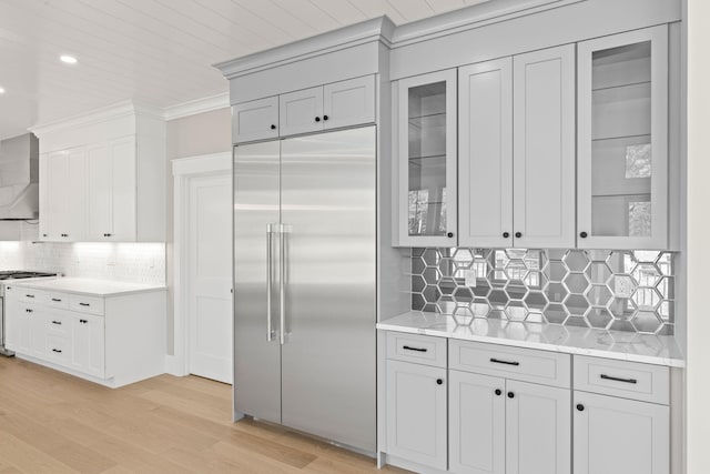 kitchen with light hardwood / wood-style flooring, backsplash, built in refrigerator, range, and wall chimney range hood