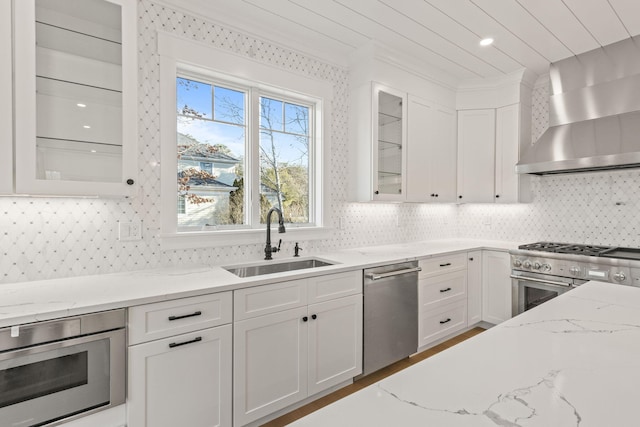 kitchen with wall chimney exhaust hood, white cabinetry, stainless steel appliances, sink, and light stone counters