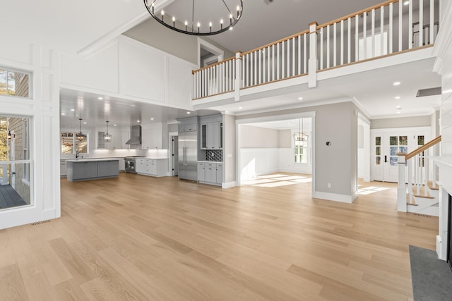 unfurnished living room with a chandelier, sink, a towering ceiling, and light wood-type flooring