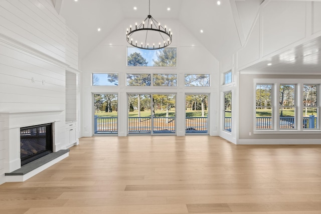 unfurnished living room featuring a chandelier, a towering ceiling, and light wood-type flooring