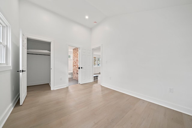 unfurnished bedroom featuring a walk in closet, light wood finished floors, high vaulted ceiling, and baseboards