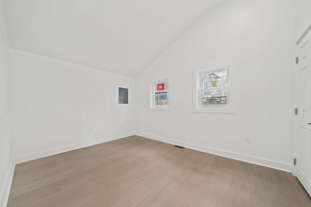 unfurnished room with lofted ceiling, light wood-style floors, baseboards, and electric panel