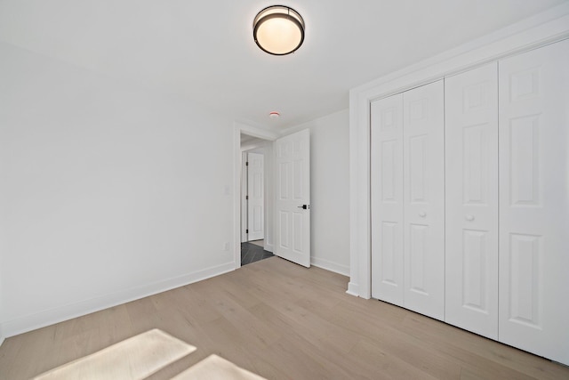 unfurnished bedroom with wood finished floors, baseboards, and a closet