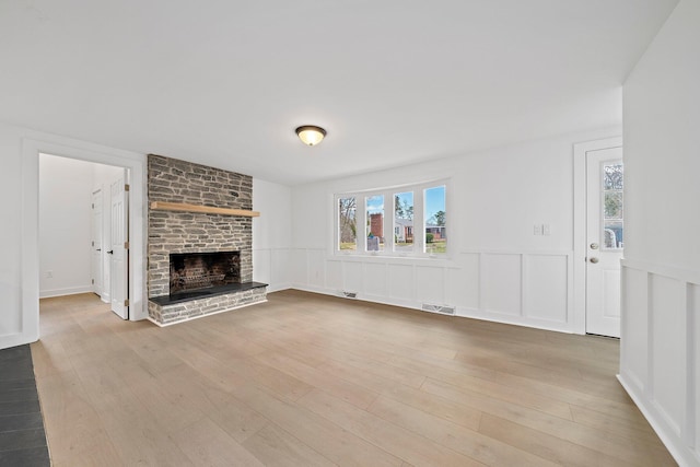 unfurnished living room featuring wainscoting, a brick fireplace, wood finished floors, healthy amount of natural light, and a decorative wall