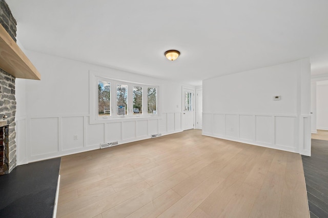 unfurnished living room with a fireplace, hardwood / wood-style floors, a decorative wall, and wainscoting