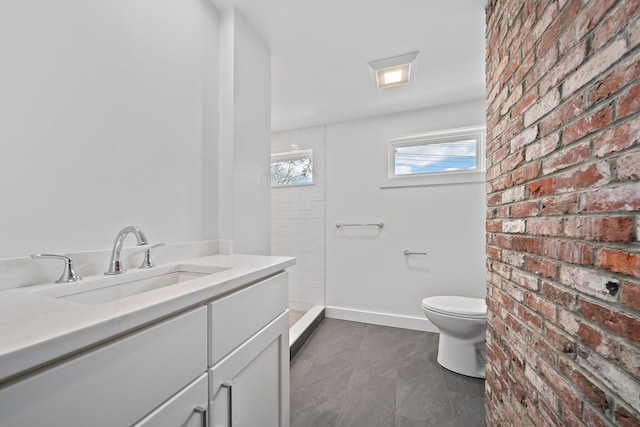 full bath with toilet, vanity, tiled shower, brick wall, and baseboards