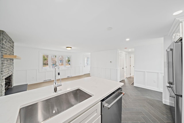 kitchen with appliances with stainless steel finishes, a sink, a decorative wall, wainscoting, and white cabinetry